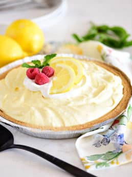 lemonade pie in a graham cracker crust and topped with lemon slices and fresh raspberries