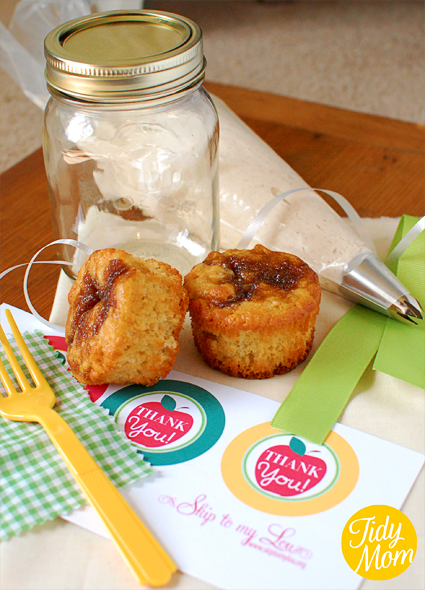 needed supplies which includes: a pint jar, two cupcakes are in the picture but you will need three, a piping bag filled with frosting, the printable tag with the words thank you on an apple on them, seven-eight grosgrain ribbon, curly ribbon, green and white gingham fabric square, and plastic fork 