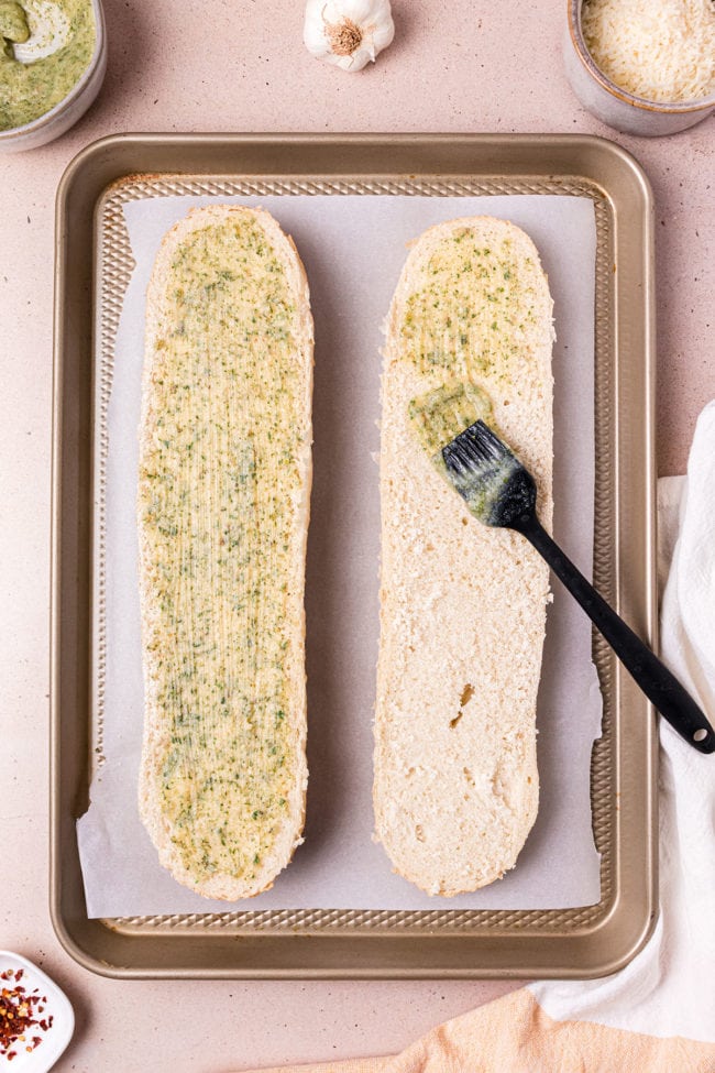 brushing seasoned butter on cut open french bread loaf