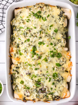 creamy chicken and spinach enchilada casserole with cheese in a white dish.