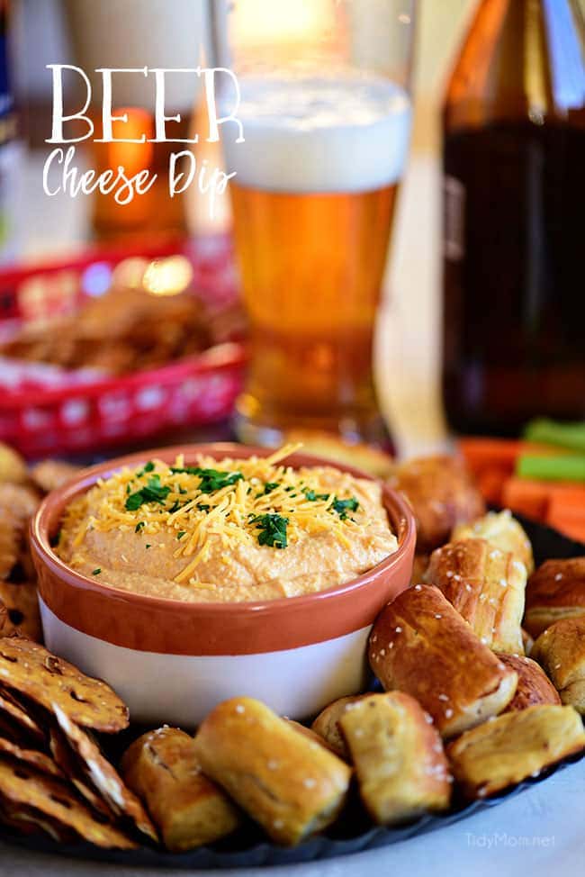 Pub-style Beer Cheese Dip on a tray in bowl with pretzel and glass of beer.