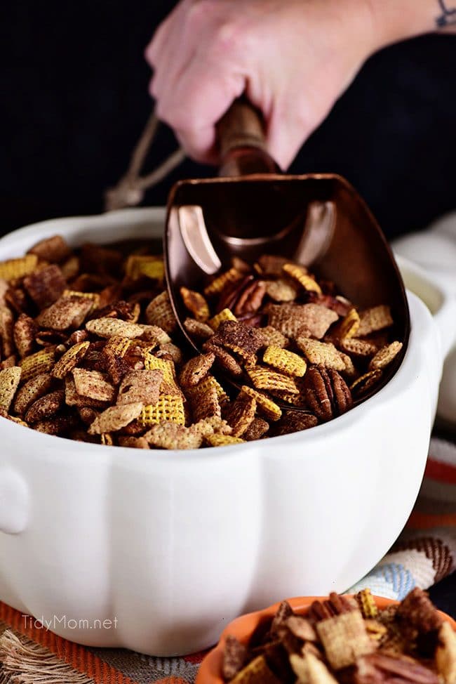 scooping chex mix out of white pumpkin bowl