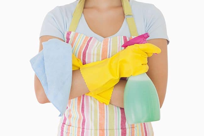 How to keep your house clean: woman holding window cleaner and rag wearing apron and rubber gloves