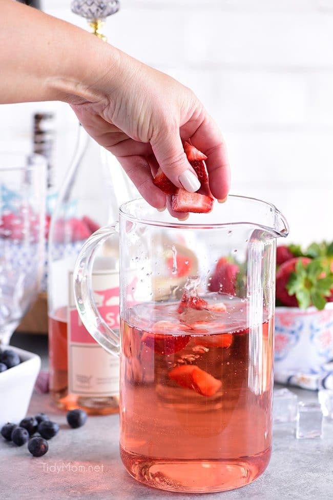 adding berries into pitcher with rosé to make a Pink Summer Sangria