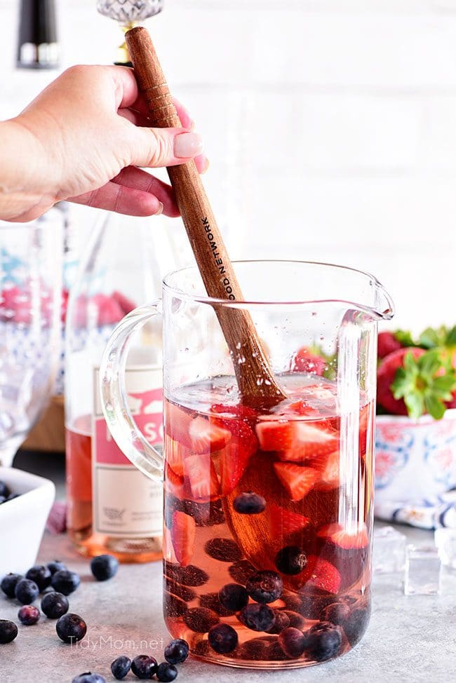 stirring pitcher of Rosé Summer Sangria with berries.