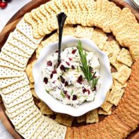 Cranberry Cream Cheese Dip with rosemary on a round tray with crackers