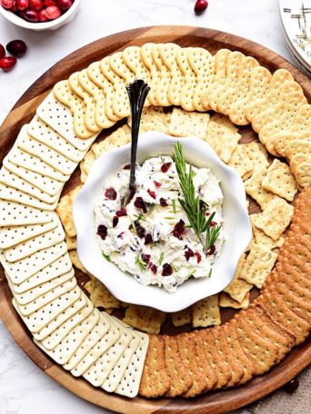 Cranberry Cream Cheese Dip with rosemary on a round tray with crackers