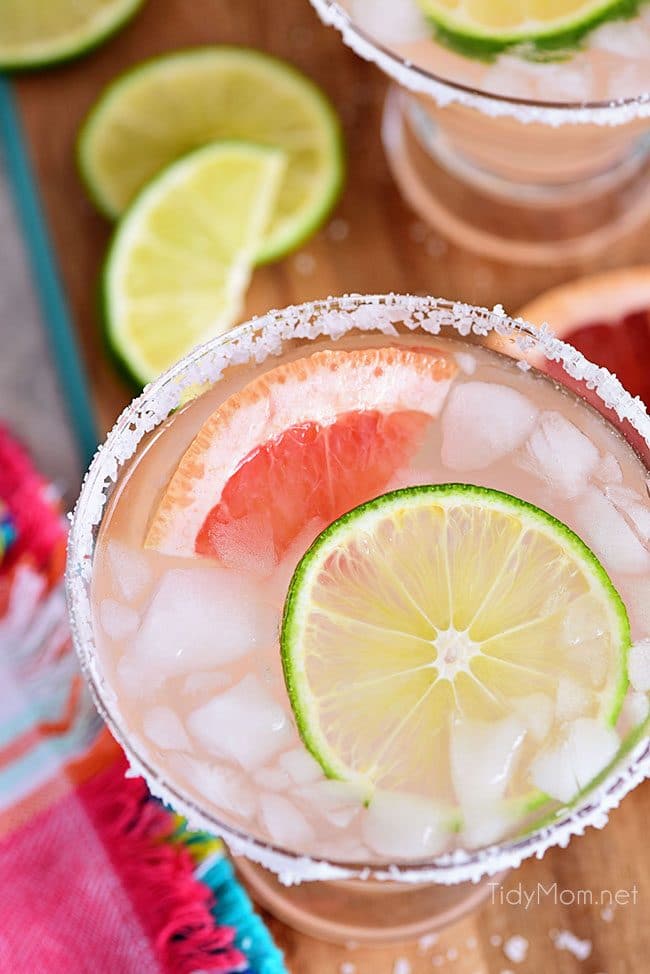 addison: A Paloma cocktail with large clear ice cubes in a tall collins  glass garnished with a grapefruit peel on a white marble counter top