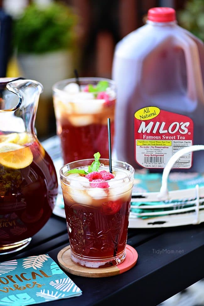 Raspberry Hard Iced Tea Cocktail in a glass with a gallon jug of Milos Famous Sweet Tea