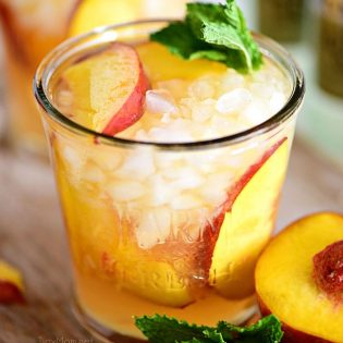 Ginger Peach Bourbon Smash cocktail on a board with a peach
