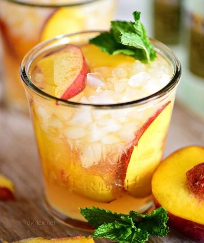 Ginger Peach Bourbon Smash cocktail on a board with a peach