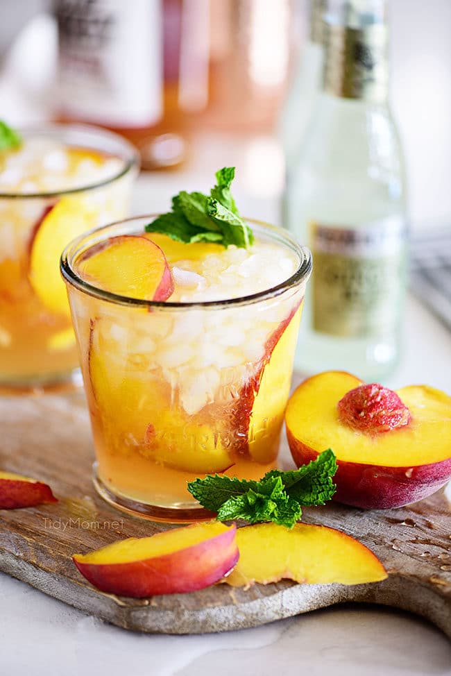 Ginger Peach Bourbon Smash cocktail on board with fresh peaches