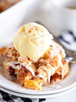 Cinnamon Roll Peach Cobbler topped with ice cream on a white plate