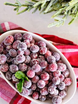 sugared cranberries in an oval bowl with Christmas napkin