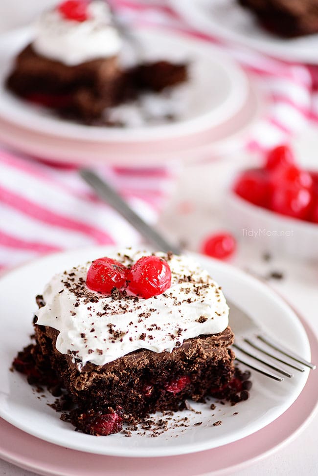 a piece of chocolate cherry cake with whipped cream and cherries on top