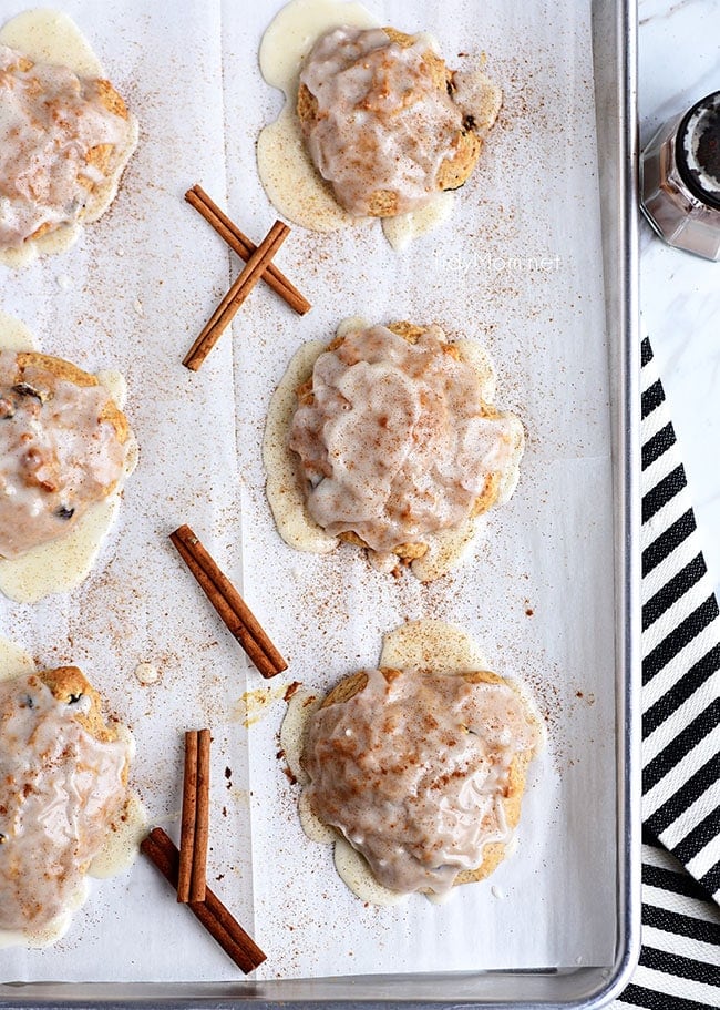 cinnamon raisin biscuits with sweet icing on a pan with cinnamon sticks