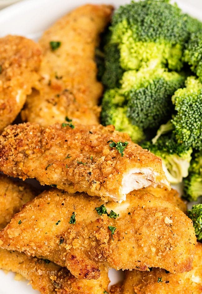 chicken tender with a bite missing on a plate with broccoli