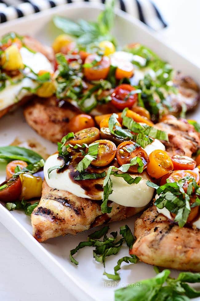 grilled chicken breasts topped with caprese salad on a white platter