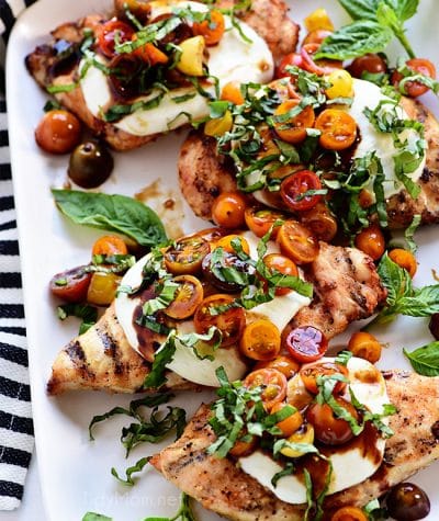 platter of grilled chicken breasts topped with caprese salad