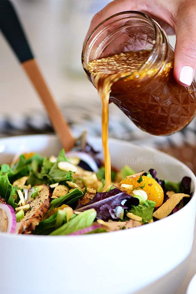 pouring Asian salad dressing over a salad