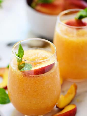 two frozen peach slush cocktails with fresh peach garnish