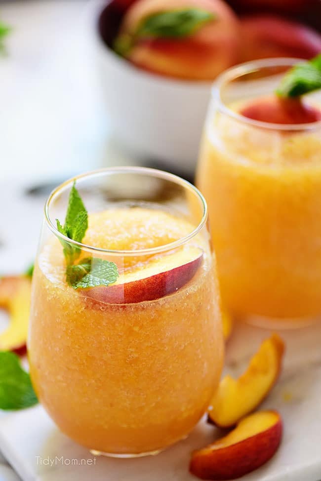 two frozen peach slush cocktails with fresh peach garnish