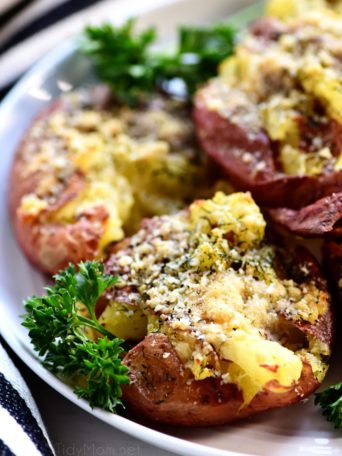 smashed potatoes with parsley garnish on a white plate