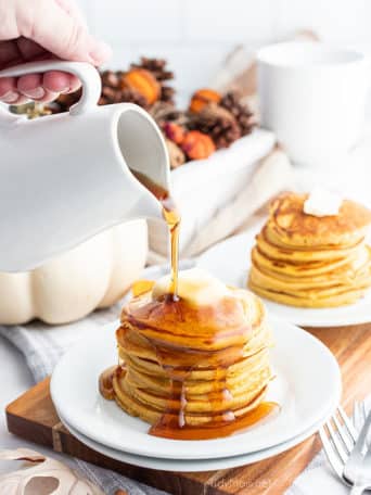 Pouring syrup on stack of pancakes with butter on plate