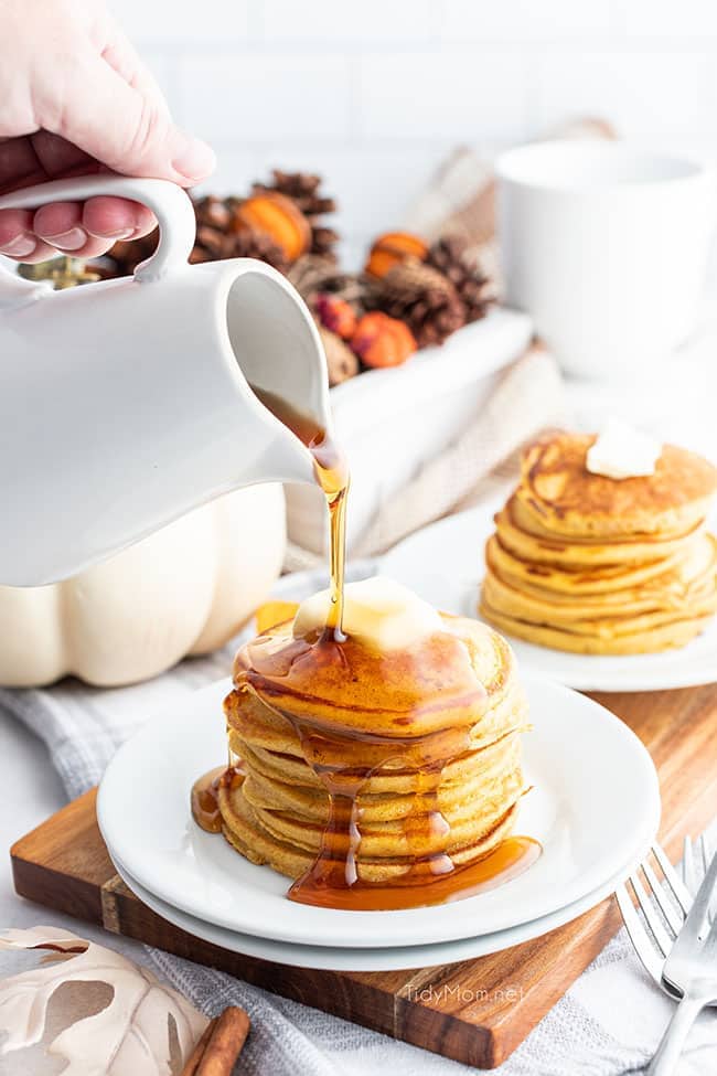 Pouring syrup on stack of pancakes with butter on plate