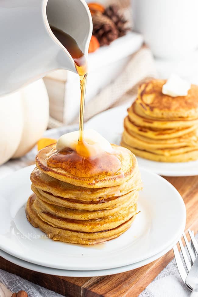 Pouring syrup on stack of pancakes on plate 