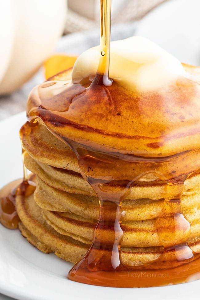 stack of pancakes on plate with syrup being poured over