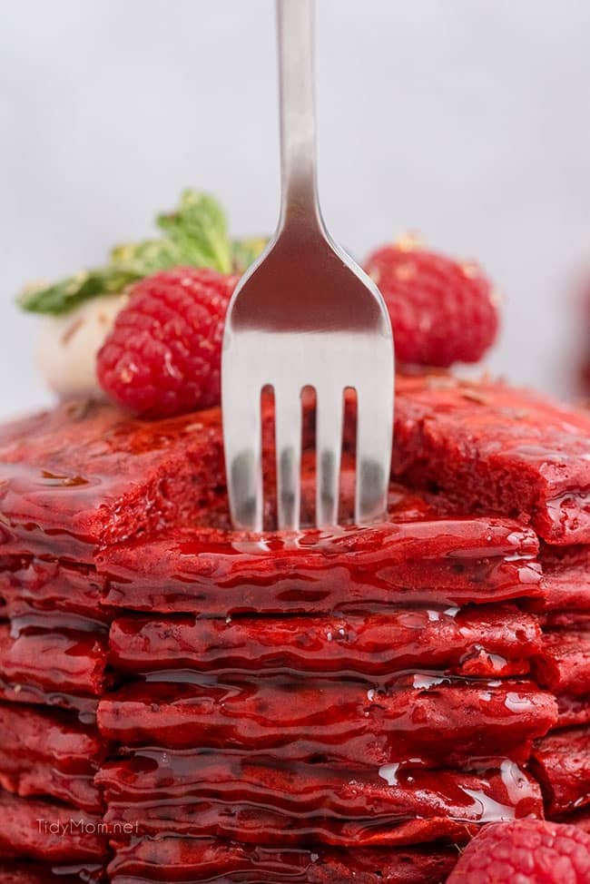 a fork going into a big stack of red pancakes
