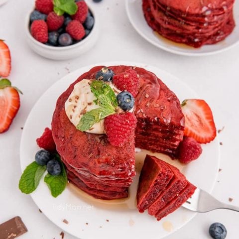 A stack of red velvet pancakes with the first bite on a fork