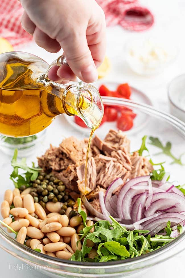 salad ingredients in a bowl and woman drizzling oil over them