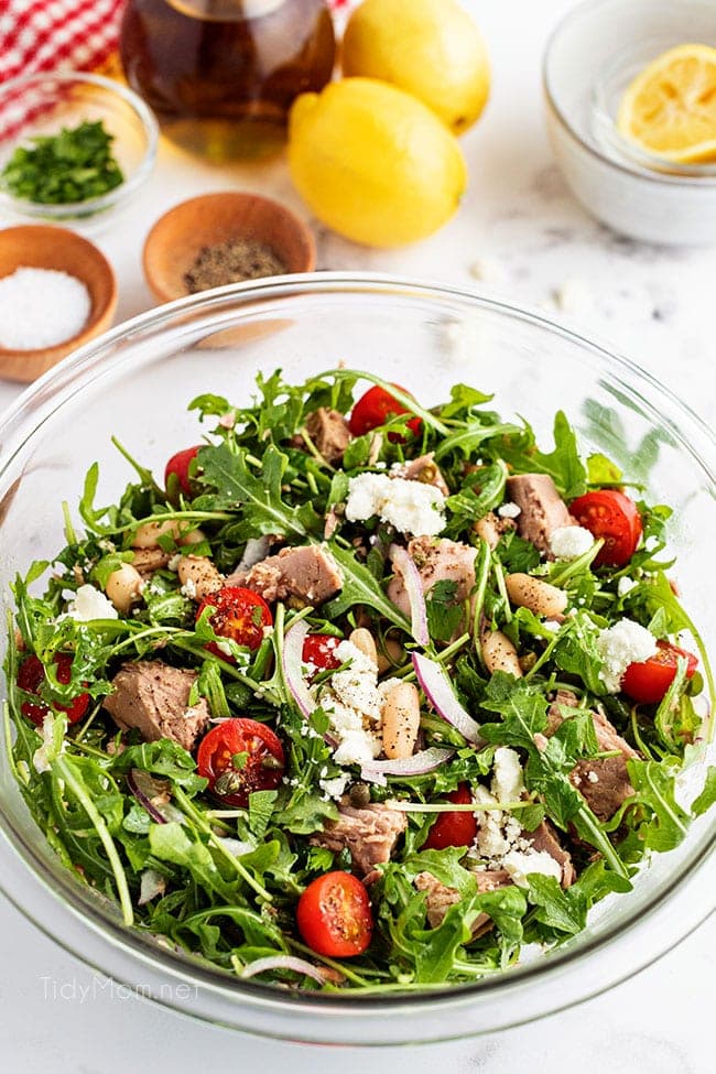 close up of salad in a glass bowl with lemons on the counter