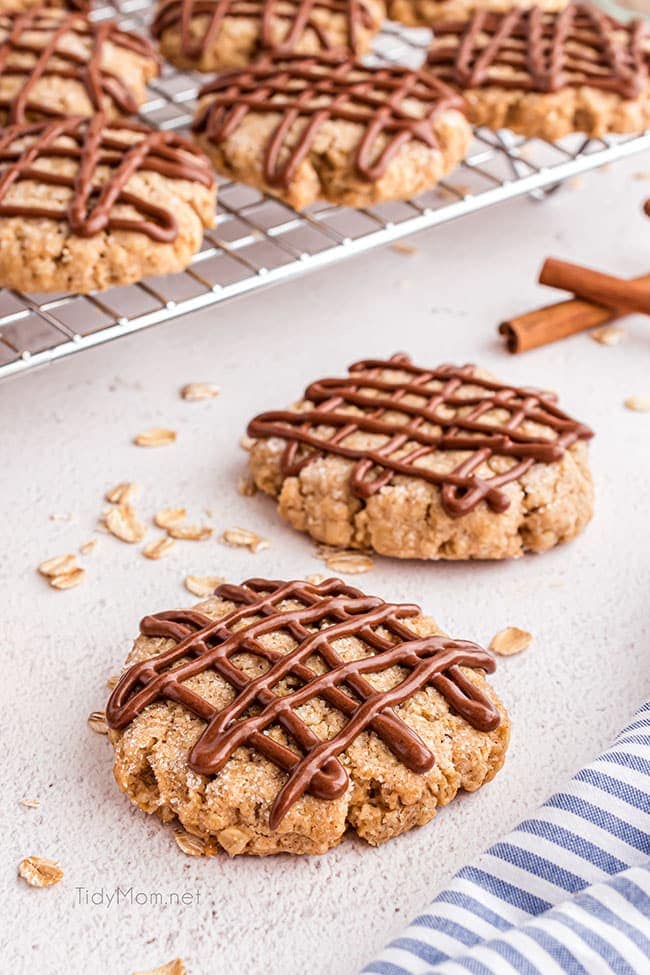 overhead shot of oatmeal cookies with chocolate drizzle on a counter with a blue stripped towel