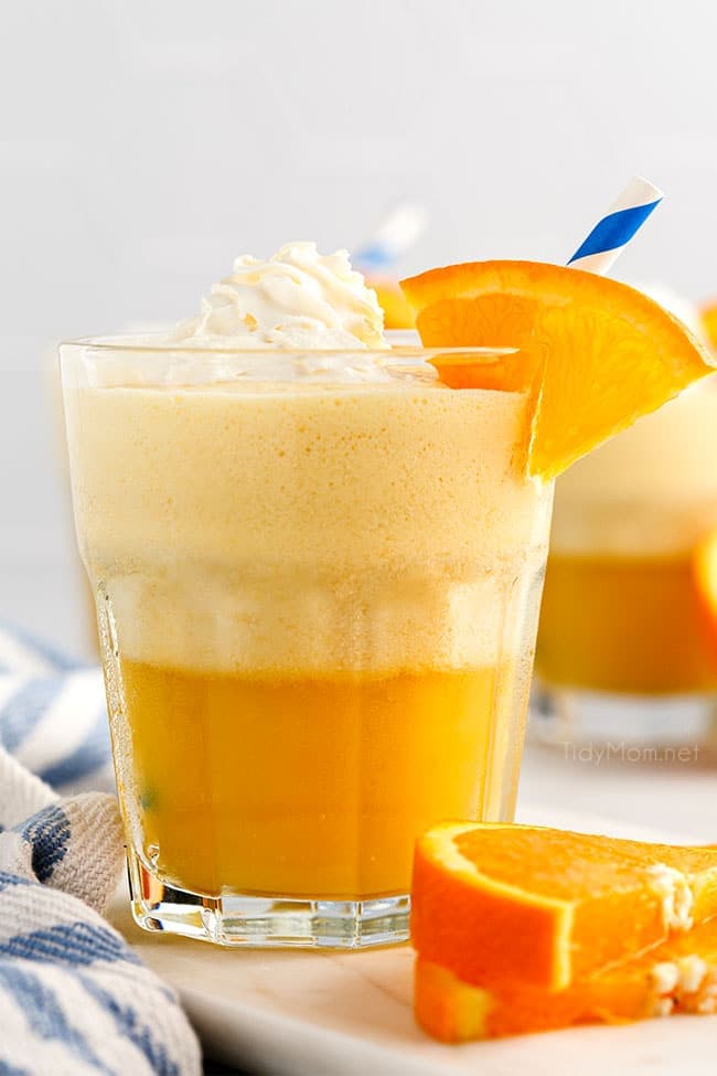 a glass fill with an Orange Julius and topped with whipped cream and fresh orange slice