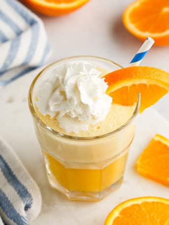 a glass fill with an Orange Julius and topped with whipped cream and a blue straw