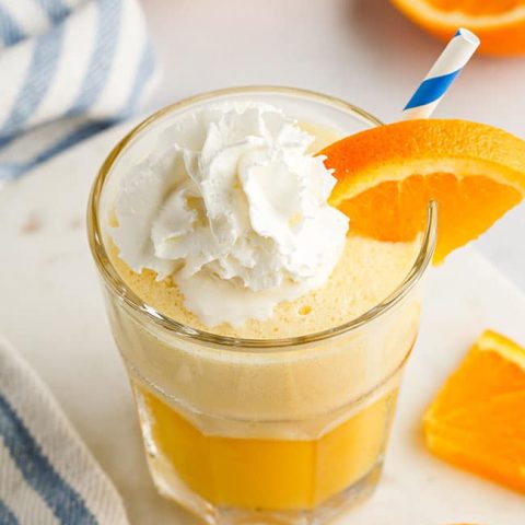 a glass fill with an Orange Julius and topped with whipped cream and a blue straw