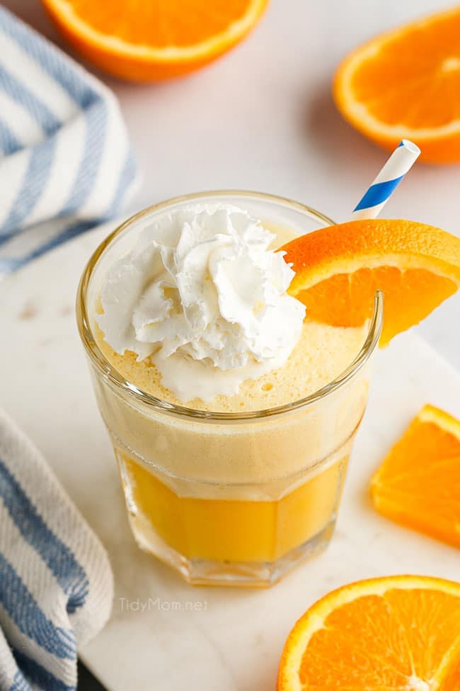 a glass fill with an Orange Julius and topped with whipped cream and a blue straw