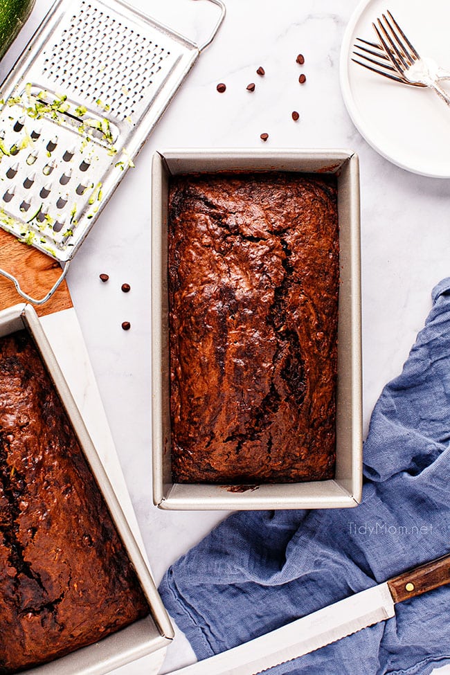 a loaf of chocolate zucchini bread in the pan with a blue towel on the counter