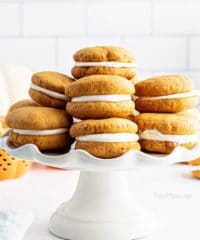 Stacked homemade pumpkin whoopie pies on a white cake stand