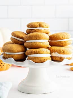 Stacked homemade pumpkin whoopie pies on a white cake stand