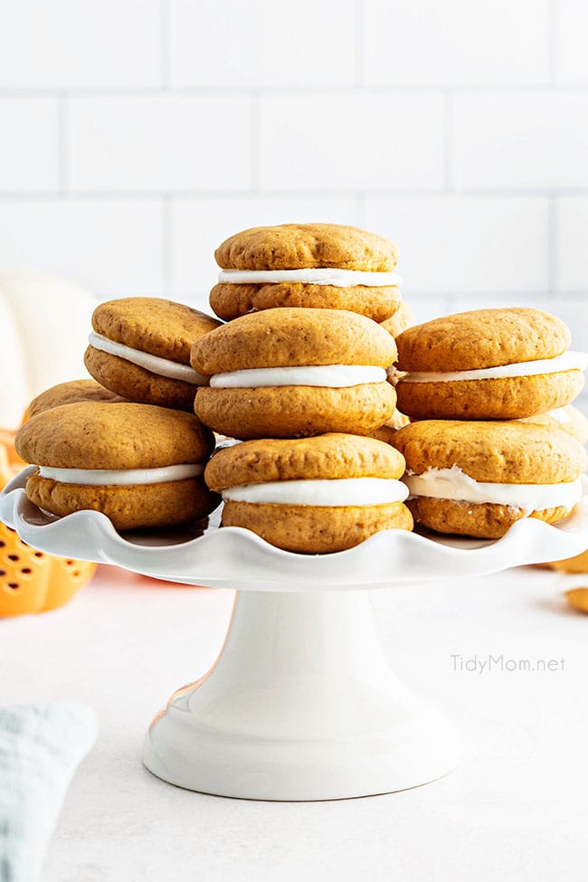 Stacked homemade pumpkin whoopie pies on a white cake stand