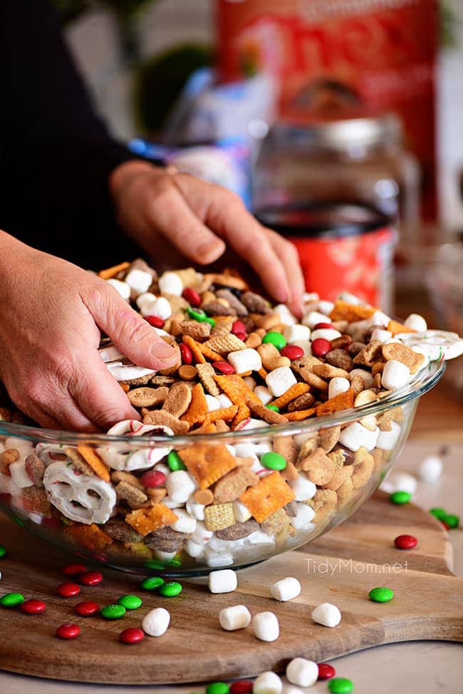 woman mixing up Christmas snack mix with her hands in a large bowl