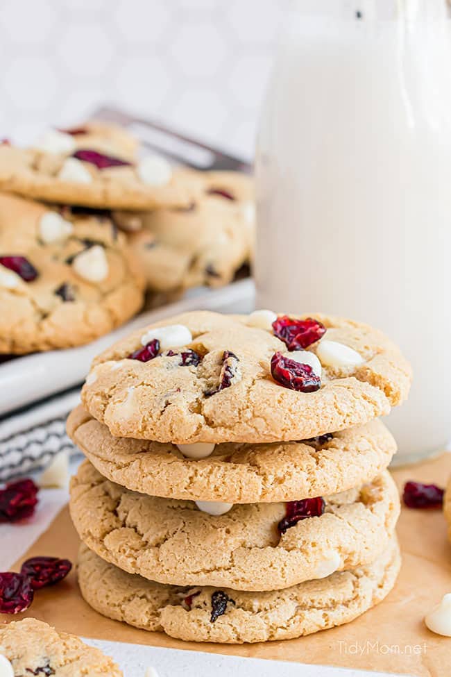 stack of four white chocolate cranberry cookies with a glass of milk
