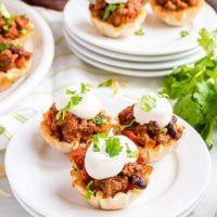 phyllo cup taco bites topped with sour cream on white plates