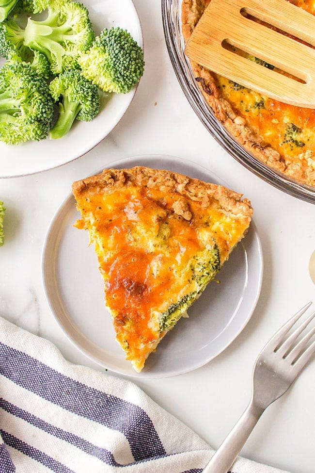Serving of broccoli cheddar quiche with frozen pie crust on a white plate