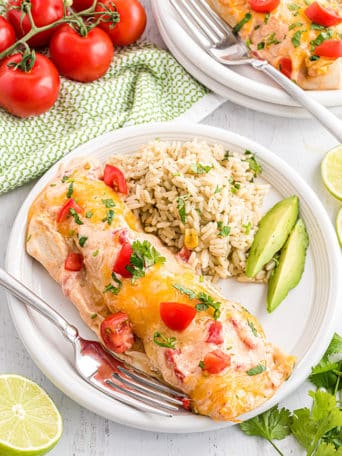 chicken and cheese enchiladas on a white plate with rice and avocados