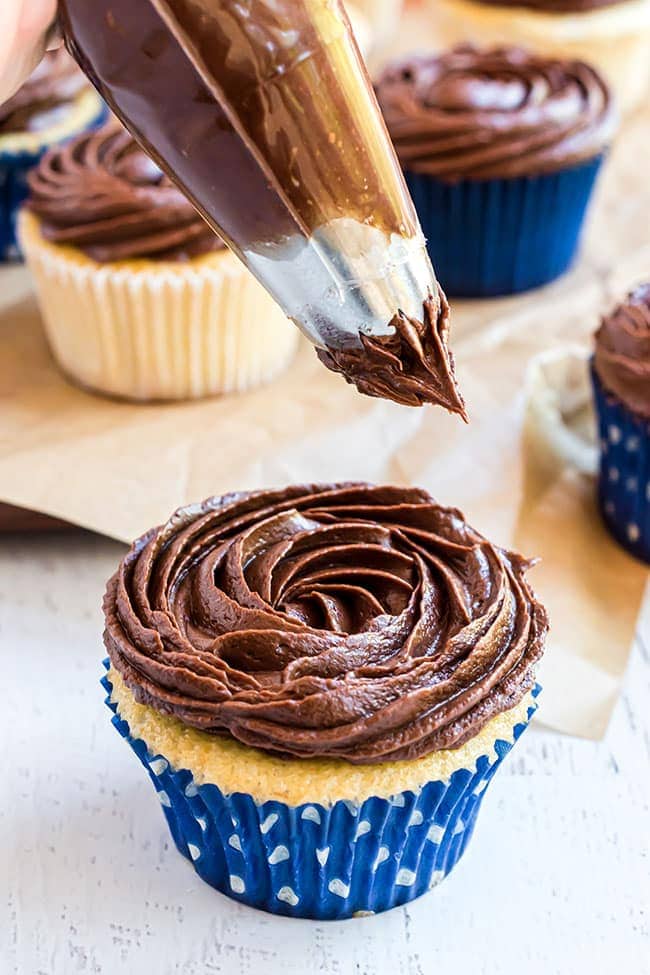 piping easy chocolate buttercream frosting on to a vanilla cupcake